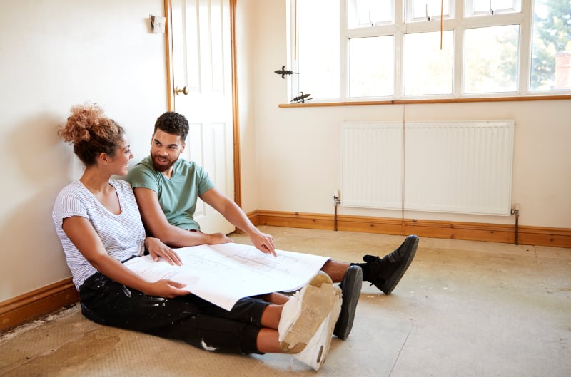 planitar couple sitting on floor looking at plans in empty 9JASQKR